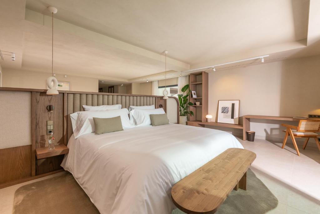 una camera con un grande letto bianco e una panca di legno di Anfitrión Villas & Suites a Marbella