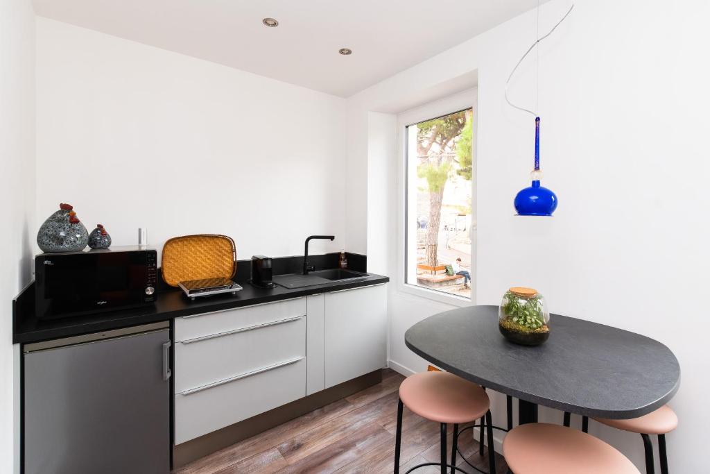 une cuisine avec des armoires blanches, une table et une fenêtre dans l'établissement Haut de Vauban, au pied de Notre Dame de la Garde - T3 Climatisé, à Marseille