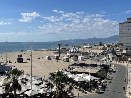 una playa con tiendas blancas, palmeras y el océano en MAGNIFIQUE VUE MER Place Centrale F2 45 m2 tout confort Travaux en cours sur façade en Canet-en-Roussillon