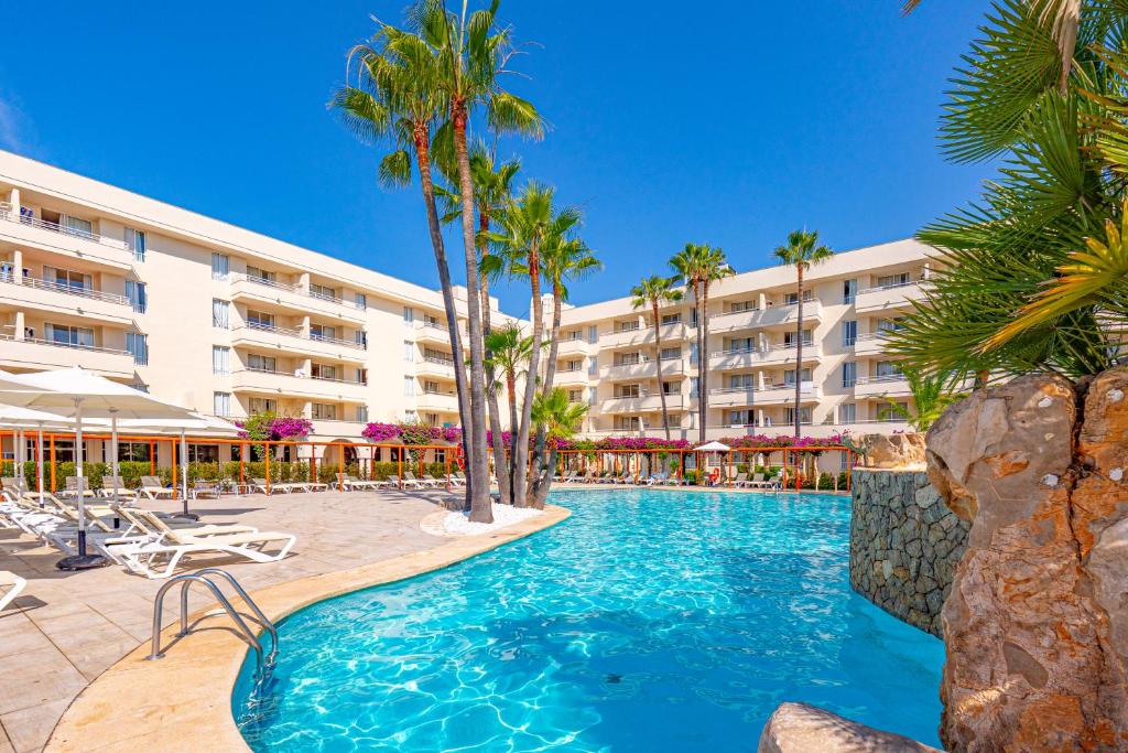 a swimming pool with palm trees and a hotel at Hotel Rosella affiliated by Intelier in Sa Coma