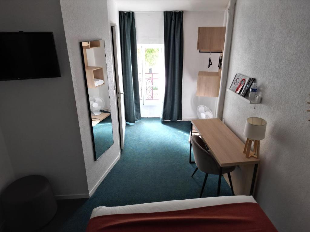 a hotel room with a bed and a desk and a mirror at Hôtel les Platanes in Villeneuve-sur-Lot
