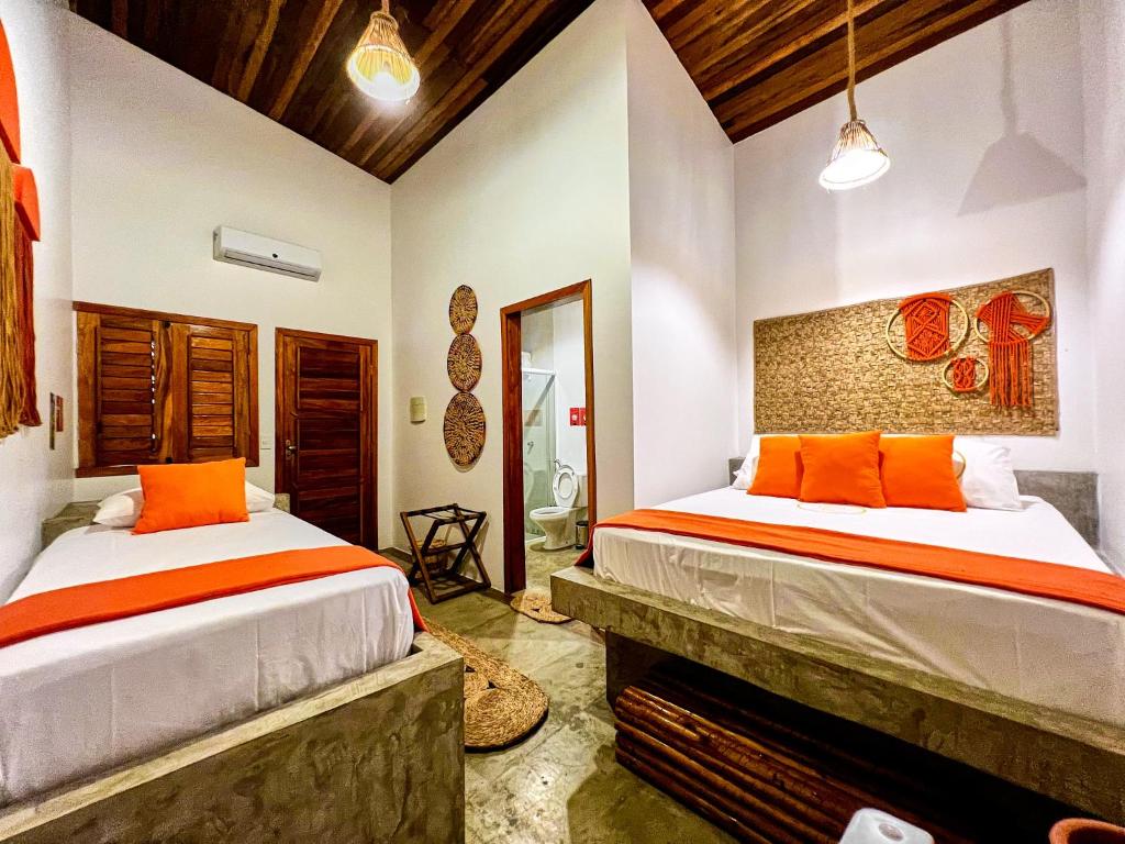 a bedroom with two beds with orange pillows at Pousada Roots - D3 Experience - Préa, CE in Prea