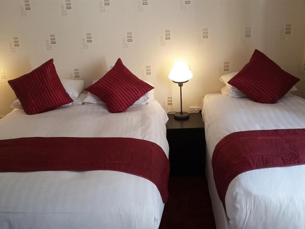 ロンドンにあるガース ホテルの赤い枕付きのベッド2台が備わる客室です。