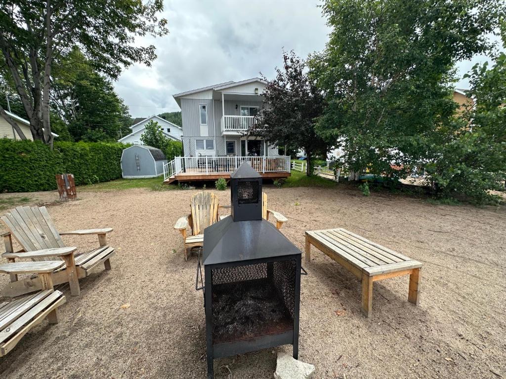 a grill with benches and a house in the background at Maison sur le lac in Desbiens