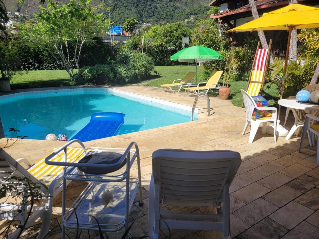 a swimming pool with chairs and a table and umbrella at Chalé Casa de Esther in Teresópolis