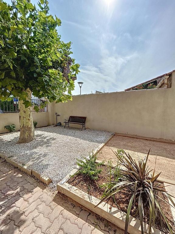 un banc assis à côté d'un mur avec un arbre dans l'établissement Charmante maison de ville avec jardin, terrasse et terrain de pétanque, à Fos-sur-Mer
