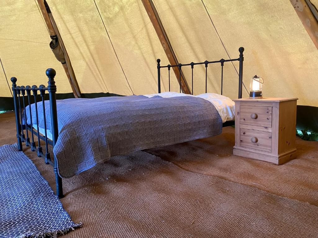 a bed in a tent with a nightstand next to it at Devon Tipi Camp And Glamp in Stoke Canon
