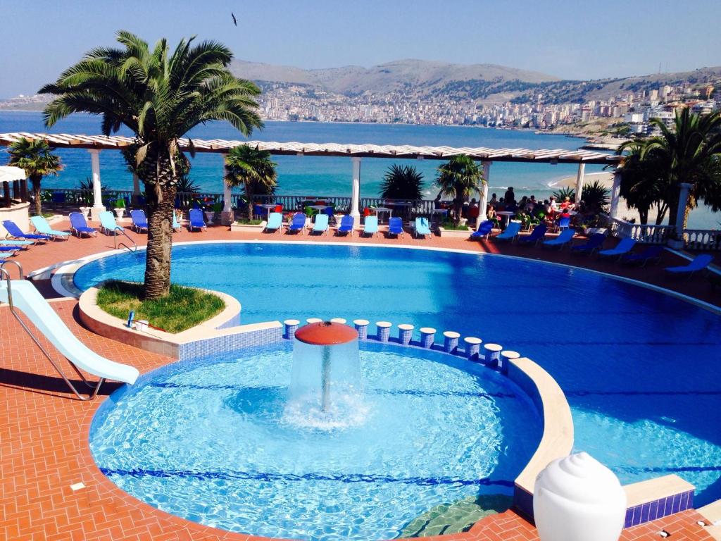 a swimming pool with a palm tree and the ocean at Hotel Dodona in Sarandë