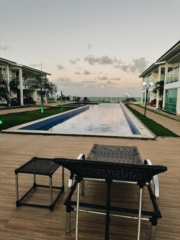 a table and chairs on a deck with a swimming pool at Bangalô duplex 602 - Riviera do Atlântico in Conde