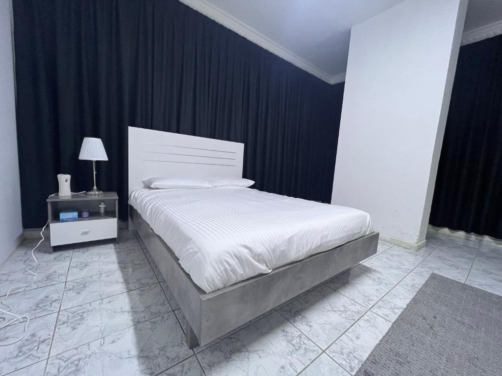 a bedroom with a white bed with a night stand at Dinar apartments in Abu Dhabi