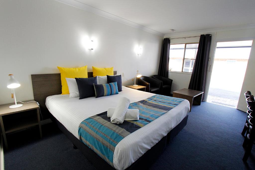 a bedroom with a large bed with yellow and blue pillows at Sugar Country Motor Inn in Bundaberg