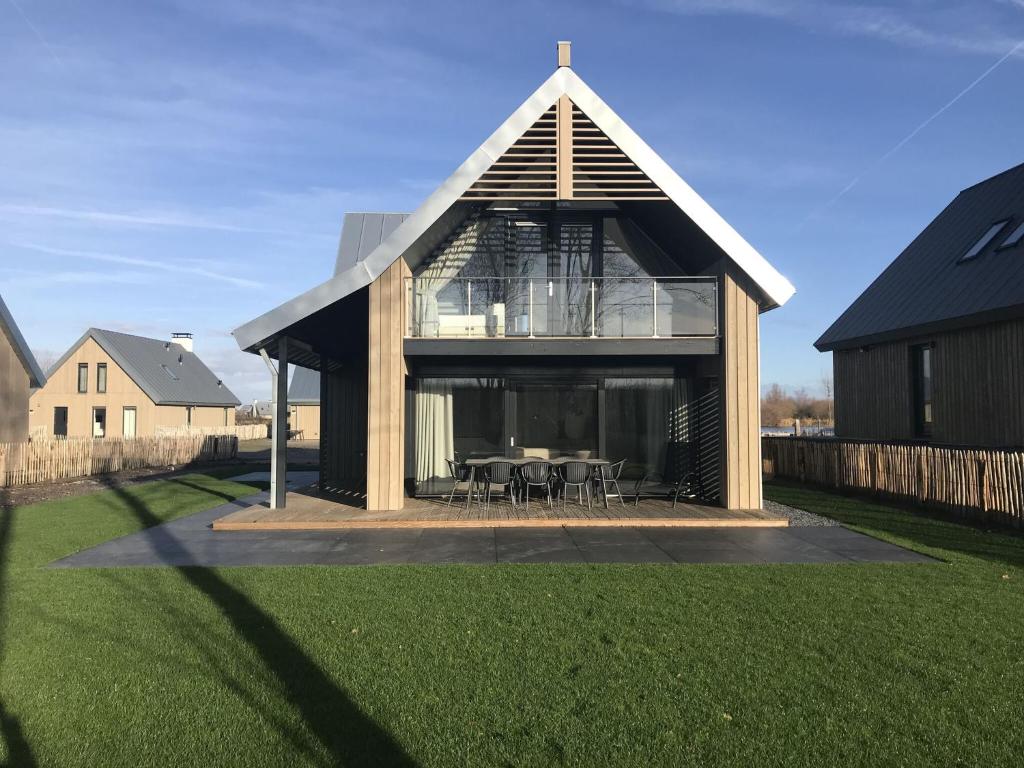 una casa con techo de gambrel con mesa y sillas en Modern design lodge directly at the water, in national park, en Tholen