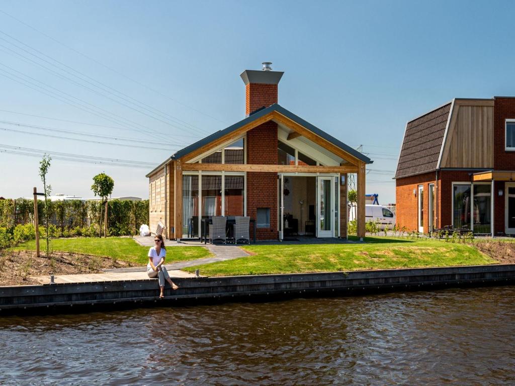 a woman sitting on a dock in front of a house at Disabled house on the water, on a holiday park in Friesland in Akkrum