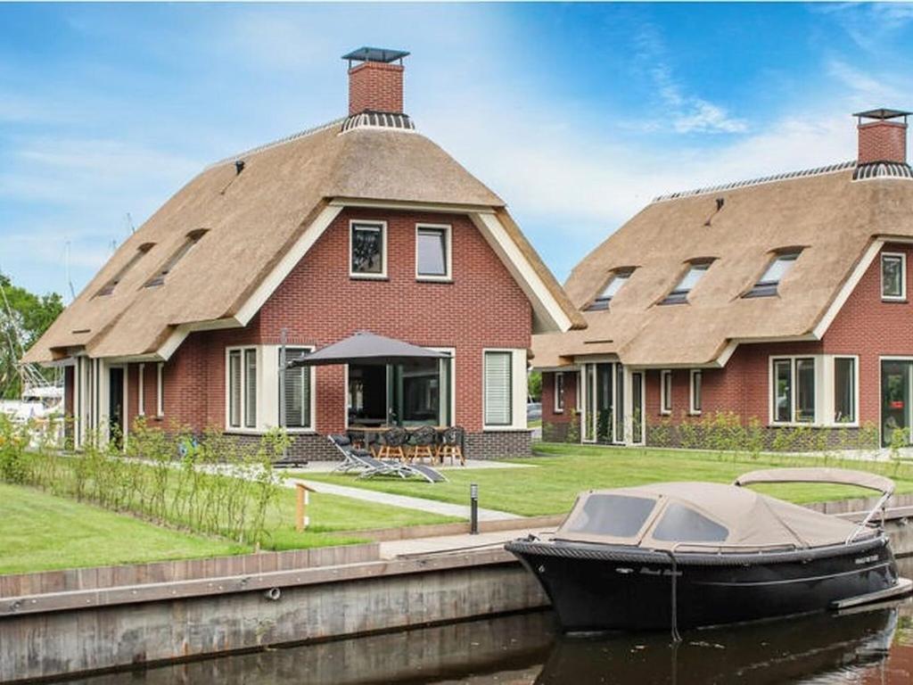 ein Haus mit einem Boot im Wasser davor in der Unterkunft Atmospheric villa with nice garden, in a holiday park at the water in Friesland in Idskenhuizen