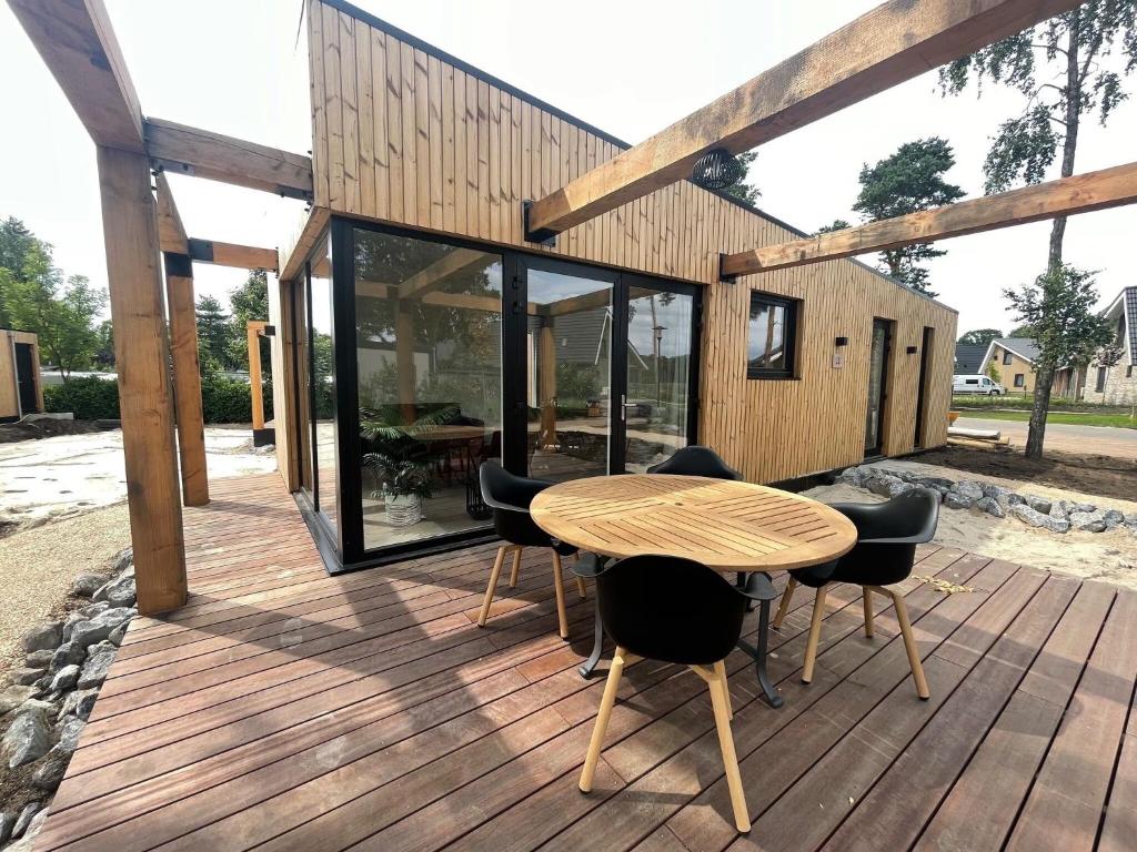 une maison dotée d'une terrasse en bois avec une table et des chaises dans l'établissement Beautiful chalet with air conditioning in a holiday park on the Leukermeer, à Well