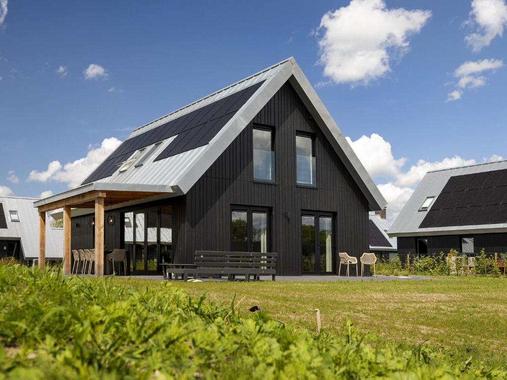 una casa negra con techo de gambrel en Beautiful villa on the water, on a holiday park in Friesland, en Sint Nicolaasga