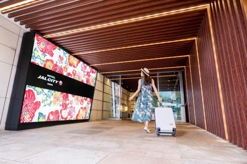 a woman walking into a building with a suitcase at Hotel JAL City Naha in Naha