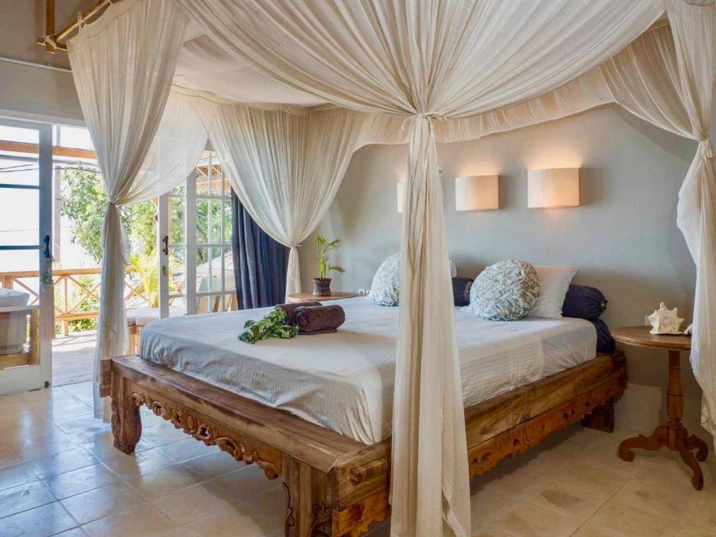 a bedroom with a canopy bed with a wooden bench at Serenity Luxurious Beachfront Villa & Spa with private Infinity Pool, 8 Guests in Gili Air