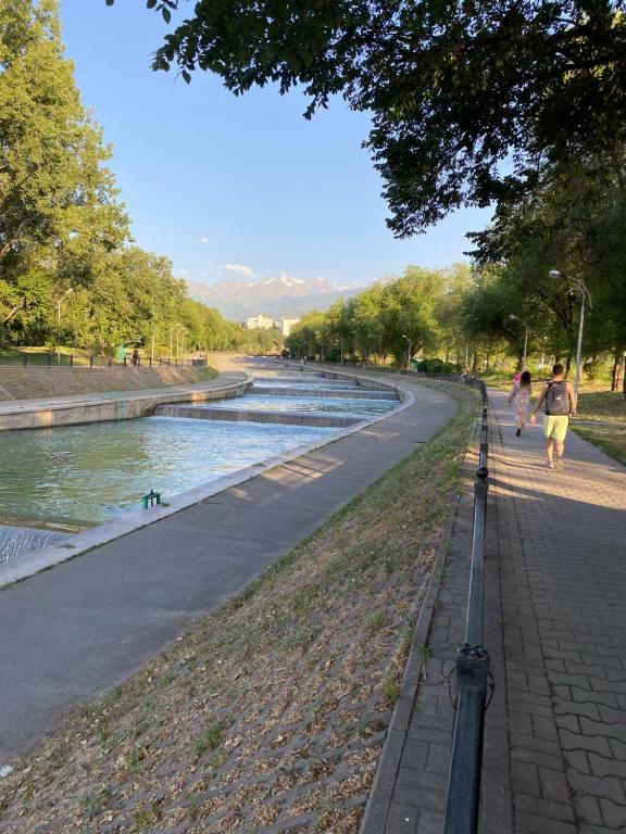 a couple of people walking down a street next to a river at Стильная студия Shadow Атакент in Almaty