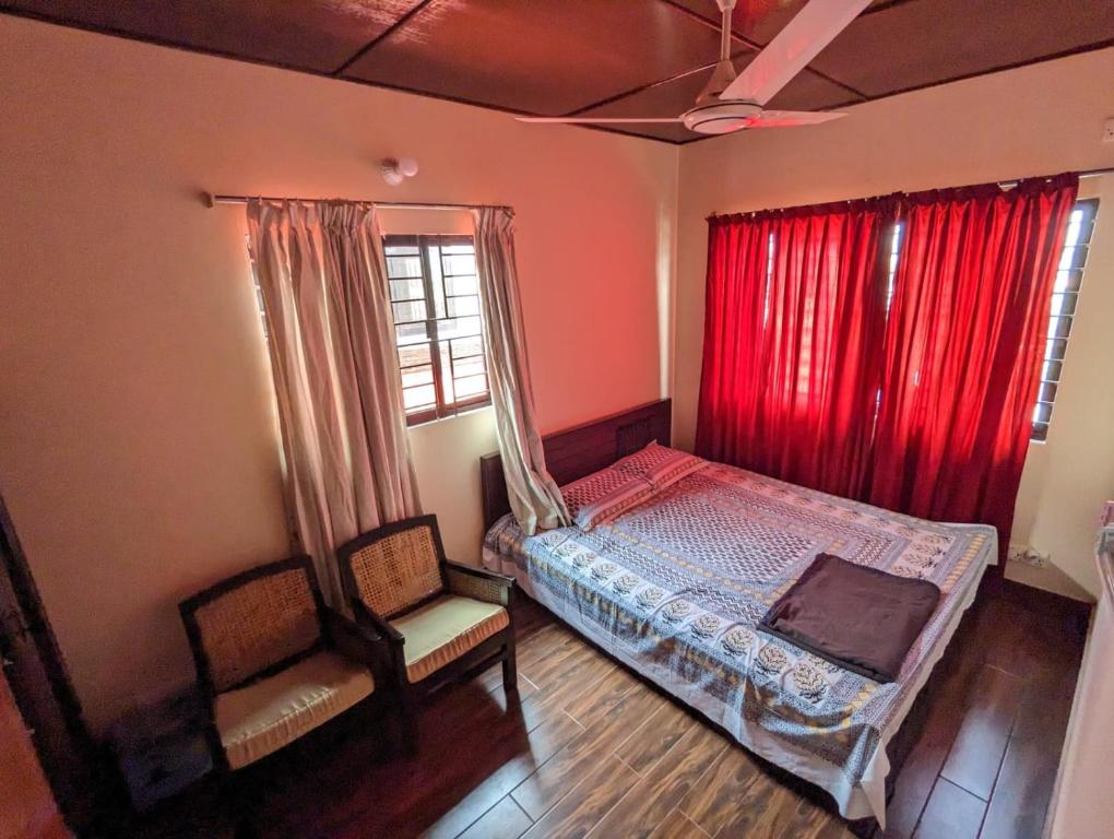 a bedroom with a bed and two chairs and red curtains at Mirabazar in Sylhet