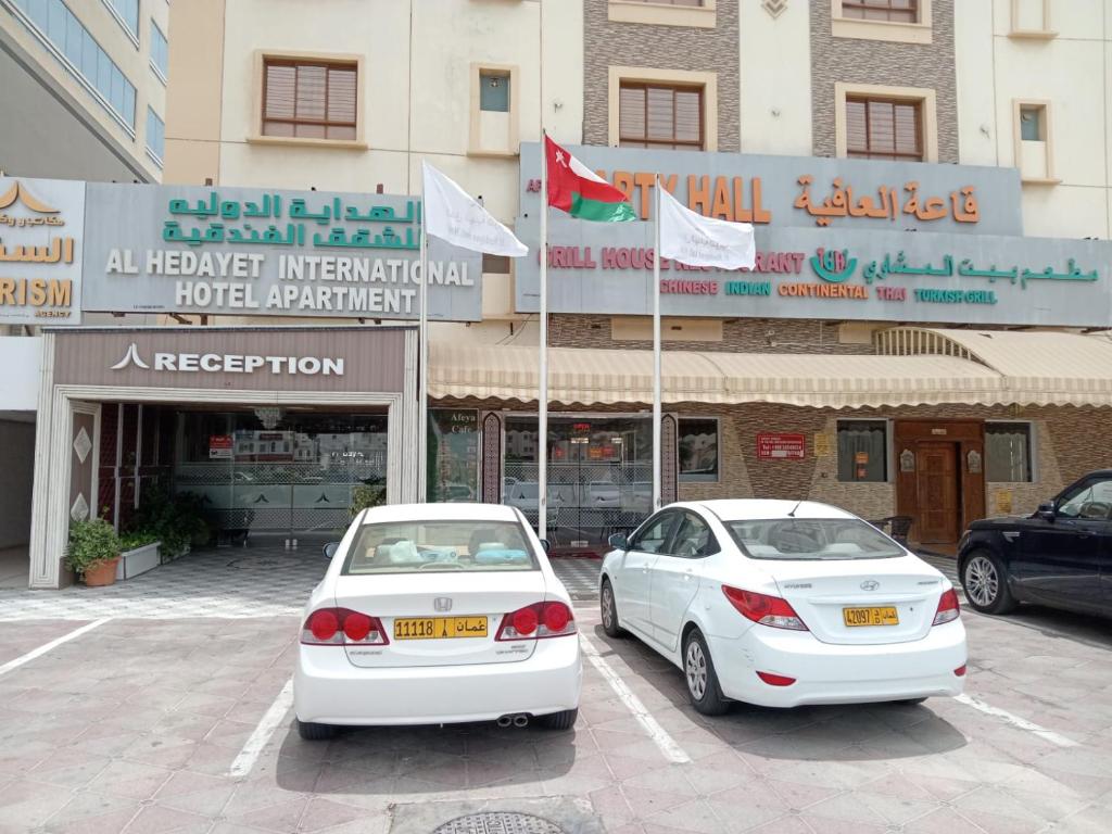 Al Hedayet International Hotel في سيب: سيارتين بيض متوقفتين امام مبنى