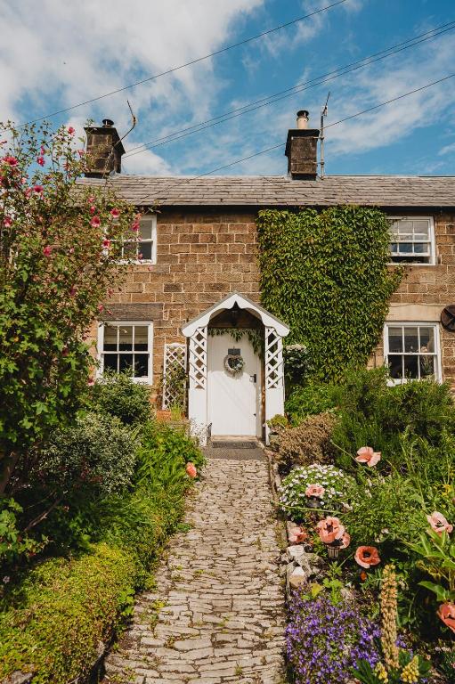 a brick house with a white door and some flowers at Swallow Cottage, Bakewell in Bakewell