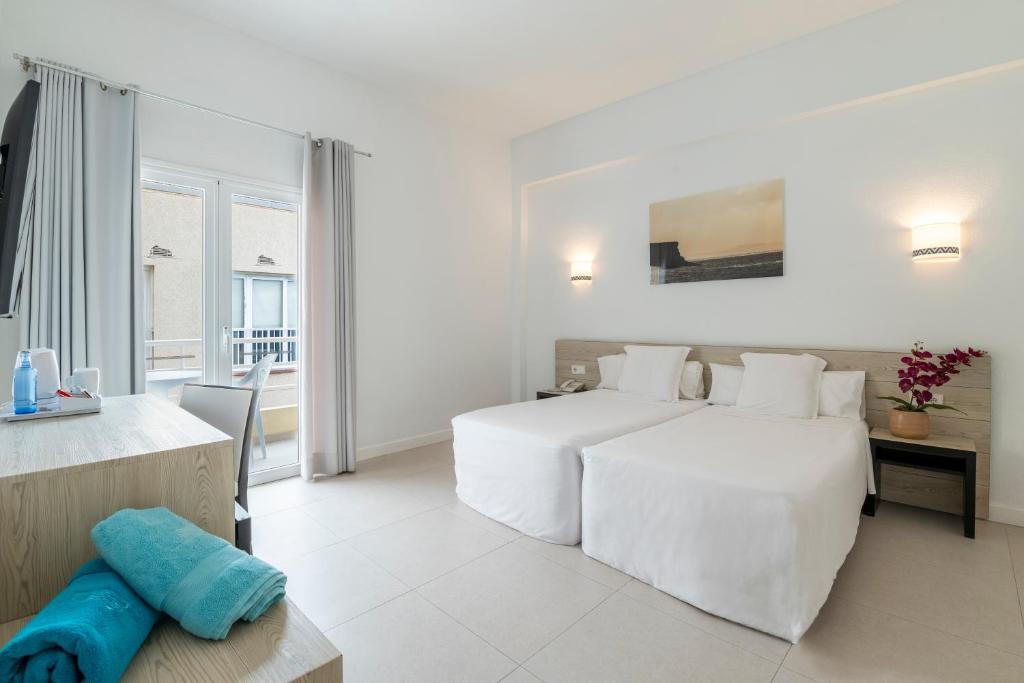 a white bedroom with a large bed and a table at Hotel Médano in El Médano