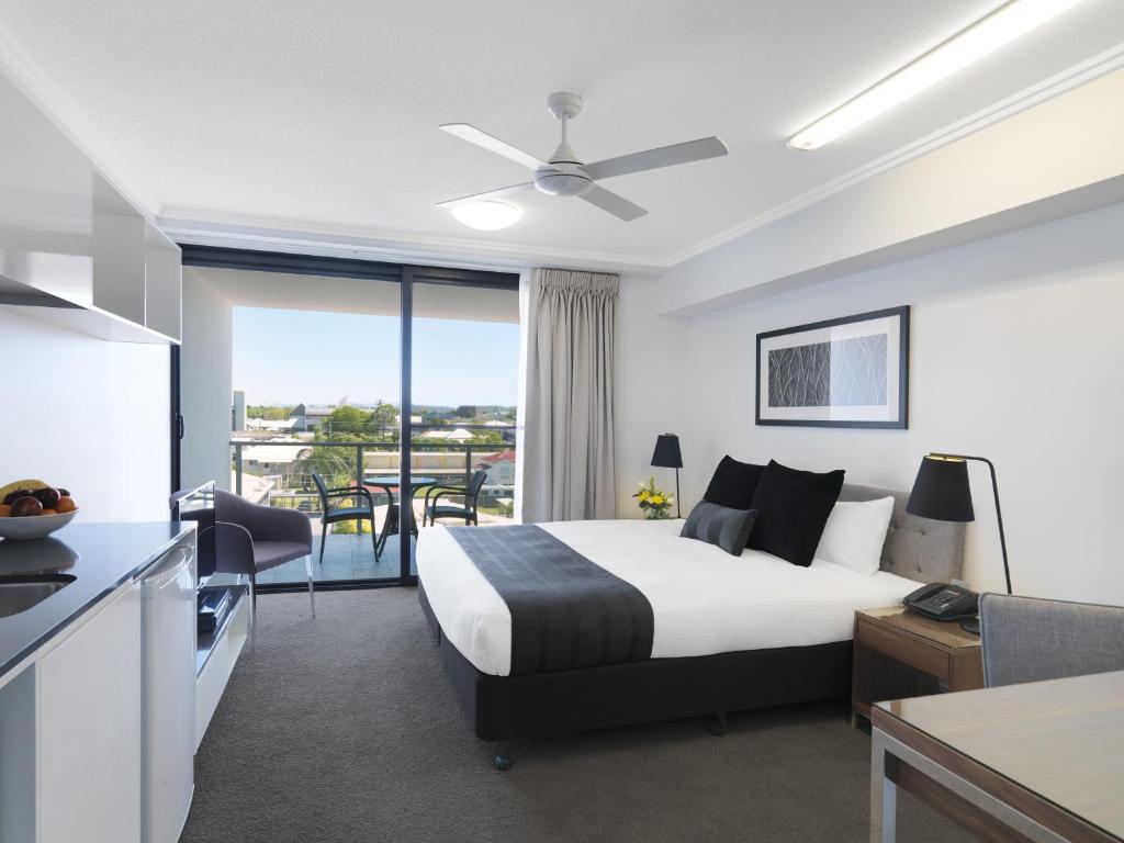 a bedroom with a bed and a kitchen with a balcony at Oaks Mackay Carlyle Suites in Mackay