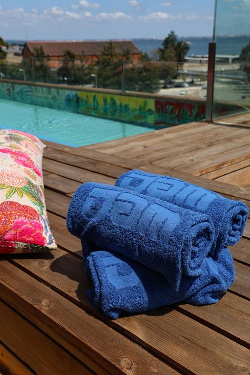 Rolled towels sit on a sunny wooden pool deck overlooking water and rooftops.