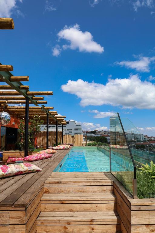 A rooftop lap pool beside a wooden deck, glass railing and panoramic city views.