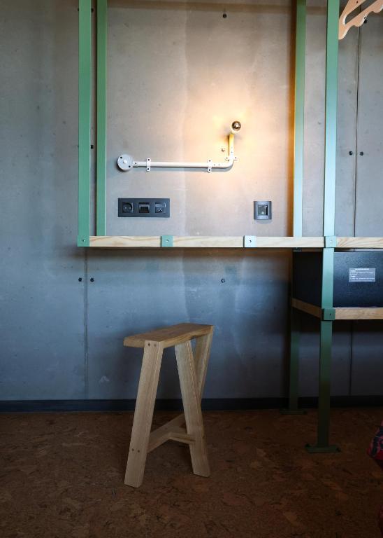 A compact industrial workspace with a wooden stool, wall light, outlets and a mounted black unit.