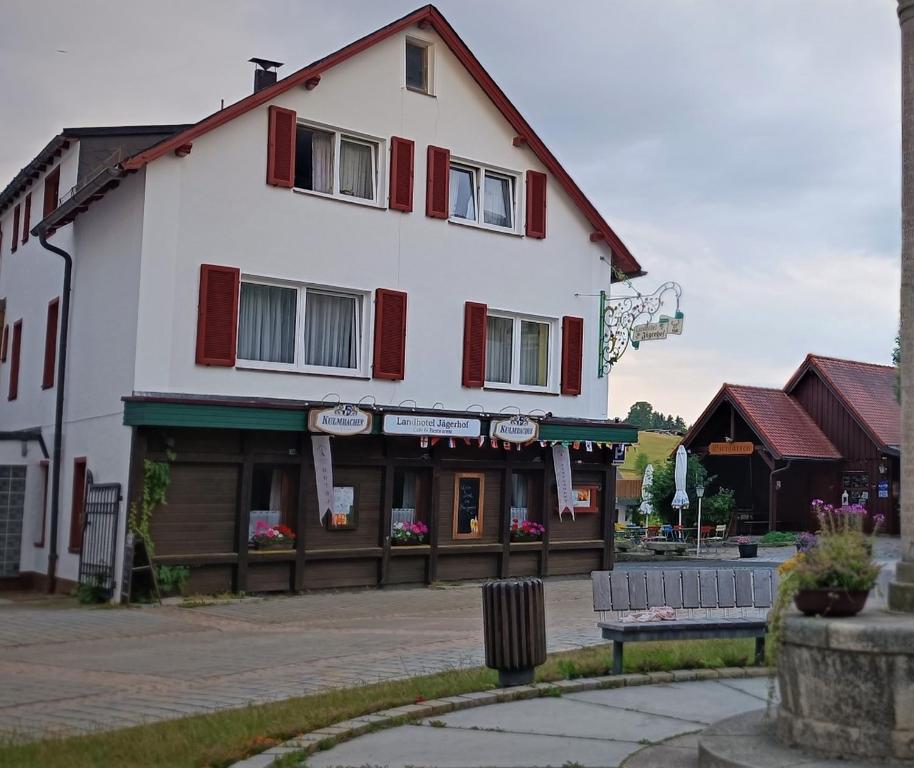 a large white building with red windows and a bench at Landhotel Jägerhof in Bischofsgrün