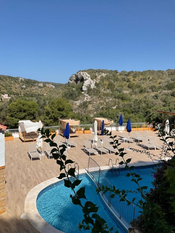 a swimming pool with chairs and umbrellas on a beach at Osprey Menorca Hotel in Cala en Porter