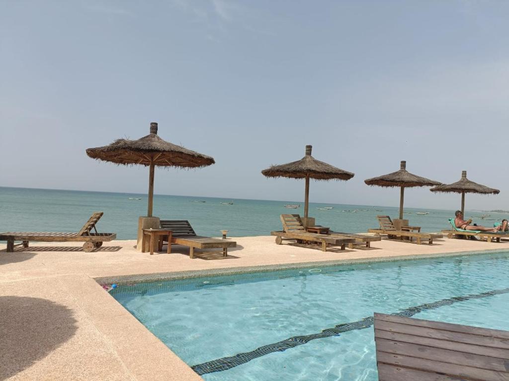 a swimming pool with chairs and umbrellas on the beach at CASA COCO II in Nianing