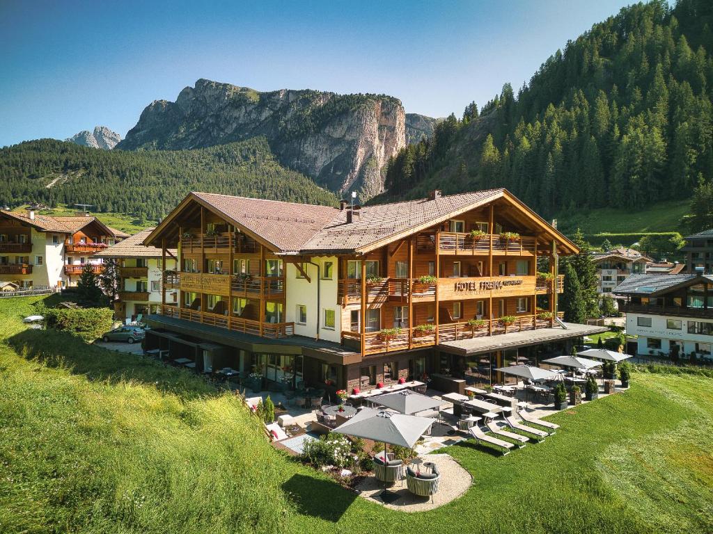 a large building with chairs and umbrellas in front of a mountain at Freina Mountain Lifestyle Hotel in Selva di Val Gardena