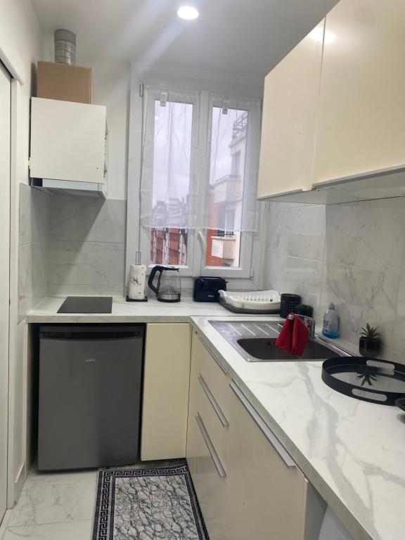 uma cozinha com armários brancos, um lavatório e uma janela em AgíaHouse - Aubervilliers em Aubervilliers
