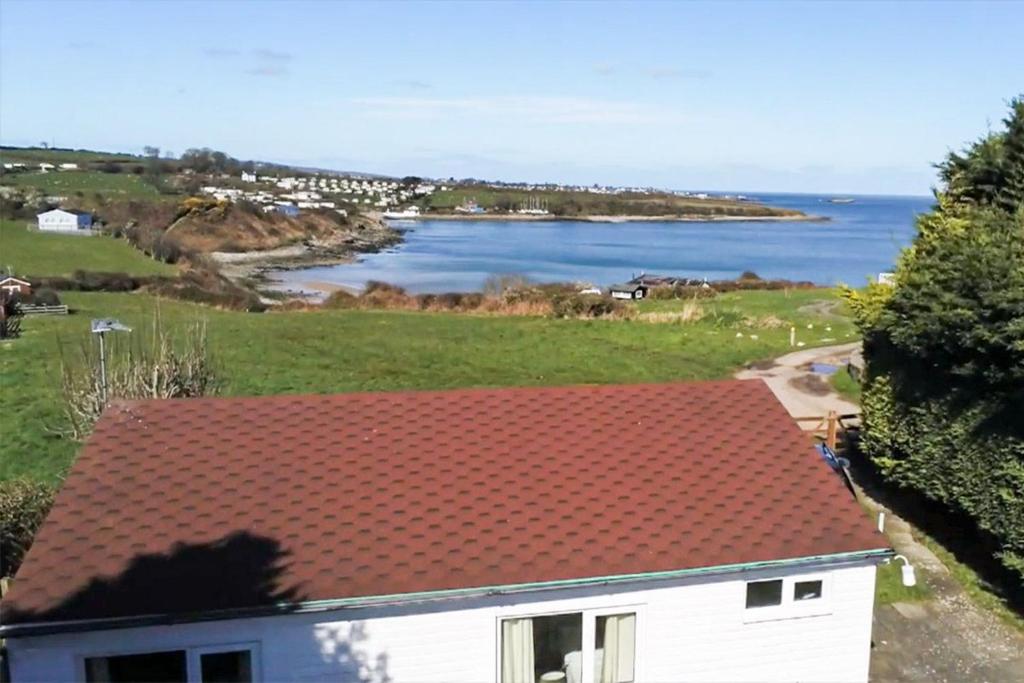 a white house with a red roof next to the ocean at Tan Dinas Lodge in Benllech