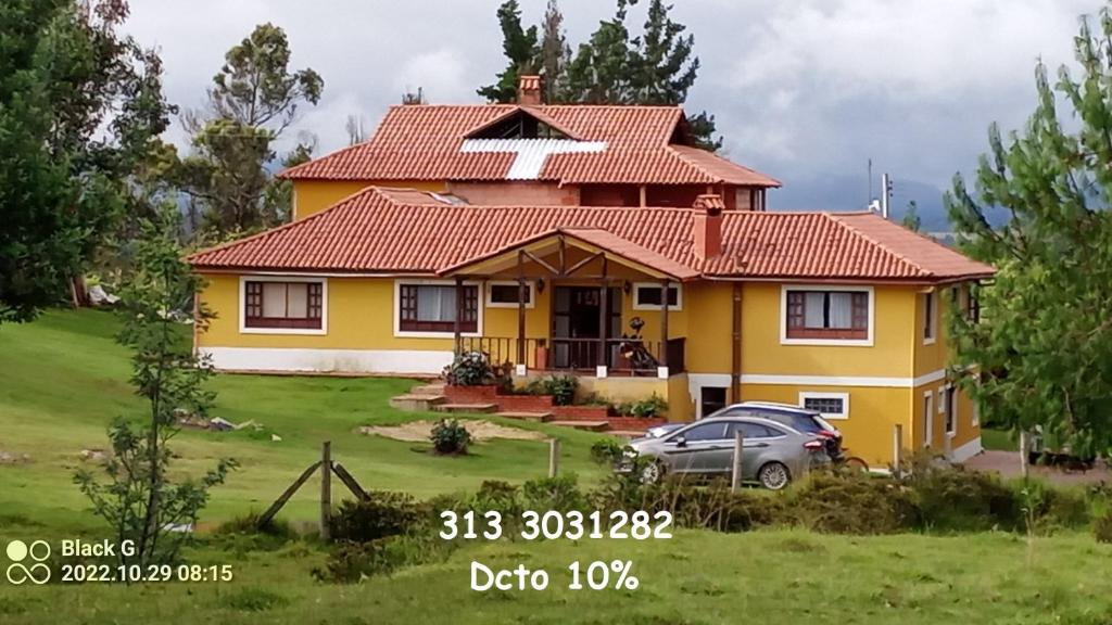 a yellow house with a car parked in the yard at Quinta Los Llanitos Hospedaje Campestre in Guatavita