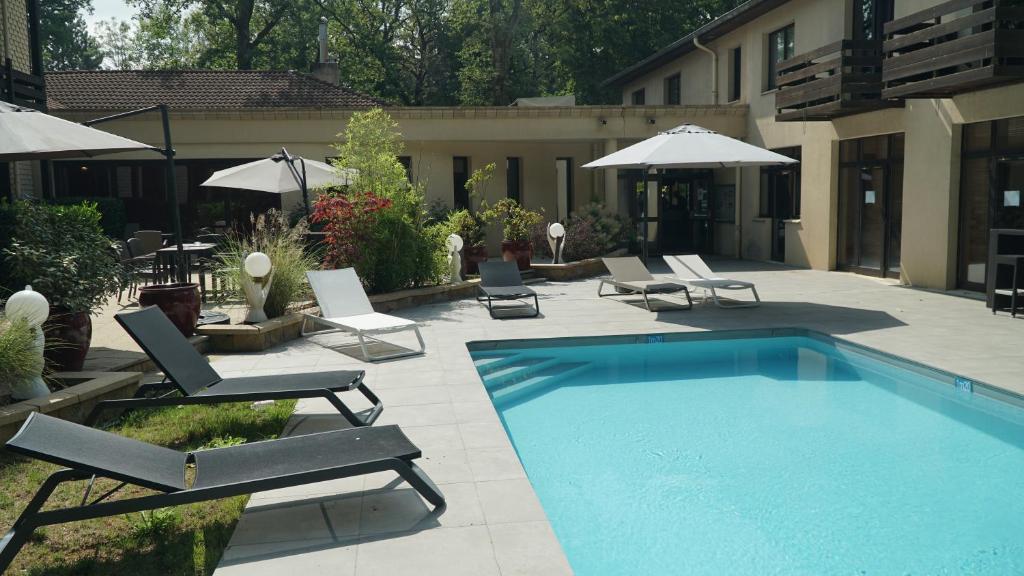 a swimming pool with chairs and umbrellas next to a building at Enzo Hôtels - ST Eloy Metz Amneville in Amnéville