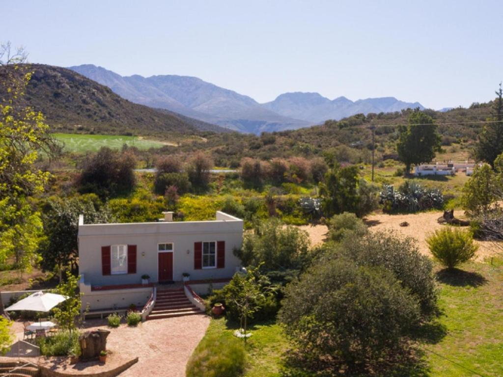 uma pequena casa branca com montanhas ao fundo em Doornkraal Tuinhuis em De Rust