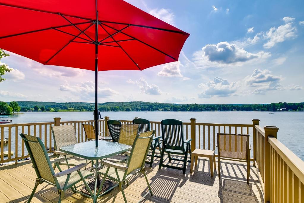 a table and chairs on a deck with a red umbrella at Cozy Cohocton Cottage with Private Beach and Deck! in Cohocton