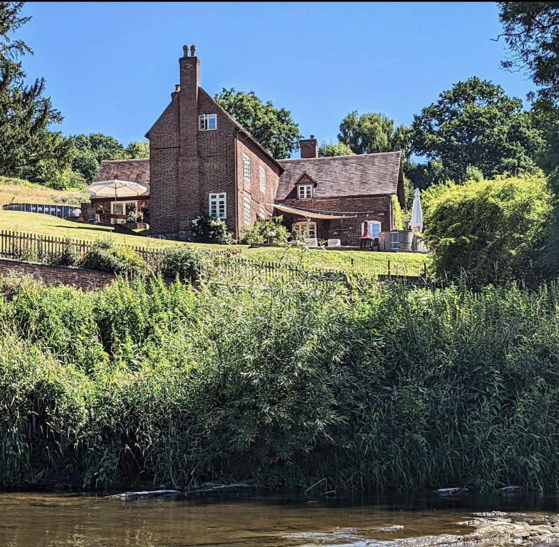 une vieille maison en briques sur le bord d'une rivière dans l'établissement Worralls Grove Guest Farm House, à Bewdley
