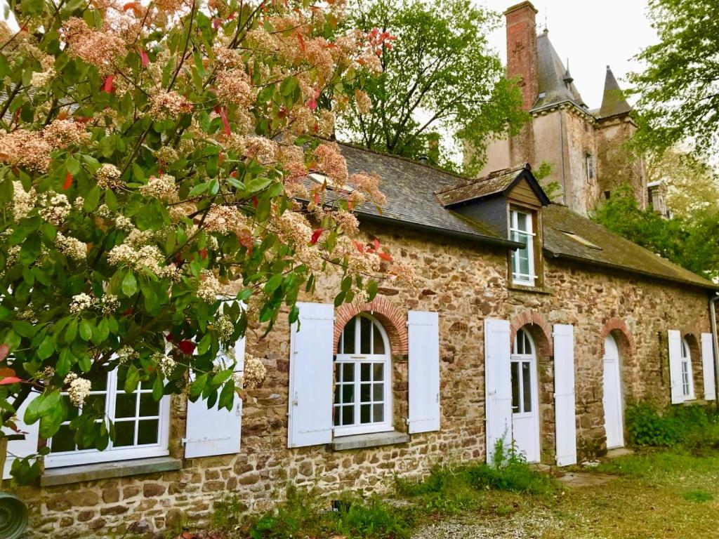 un vieux bâtiment en briques avec des fenêtres blanches et un arbre dans l'établissement Cottage du château, à Erbrée