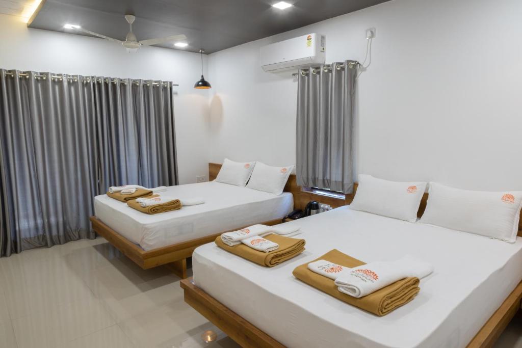 two beds in a room with white walls and curtains at Coco Palms Inn in Alibaug