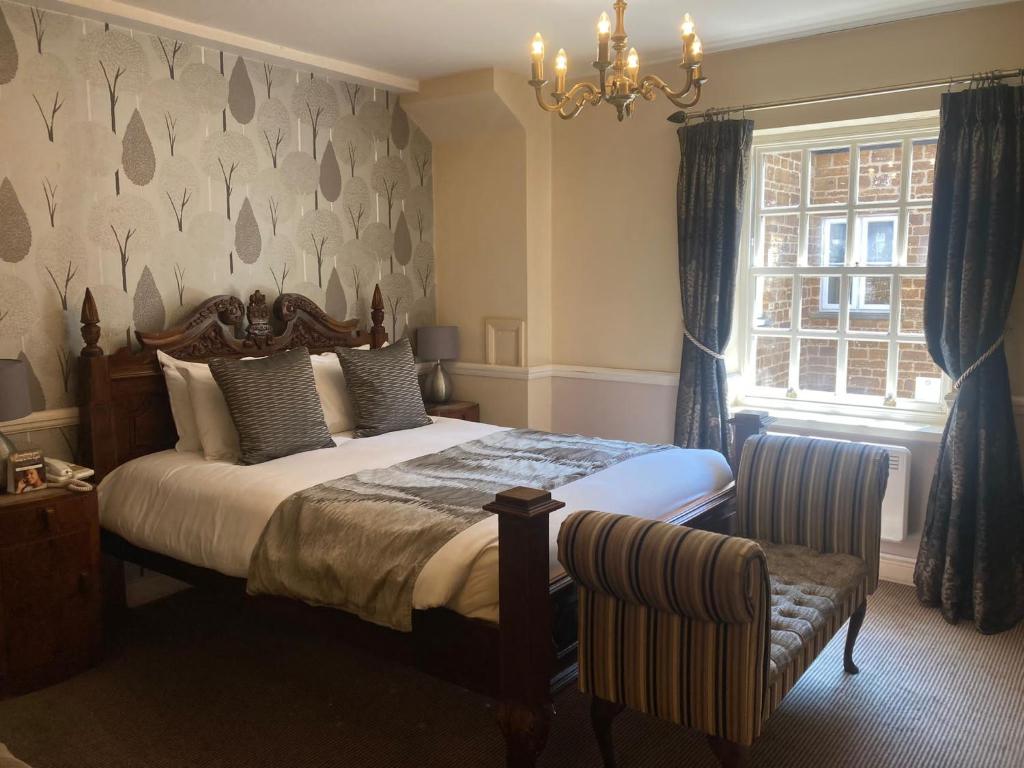 a bedroom with a bed and a window and a chandelier at Saracens Head Hotel by Greene King Inns in Towcester