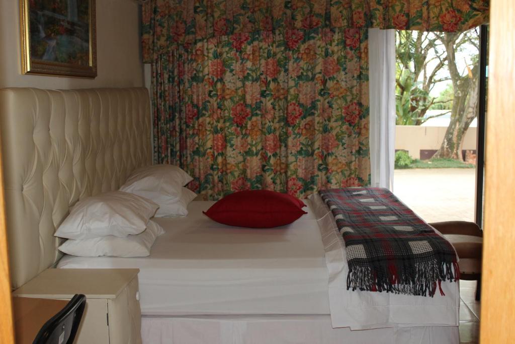 a bed with a red pillow and a window at Tzaneen Guest House in Tzaneen