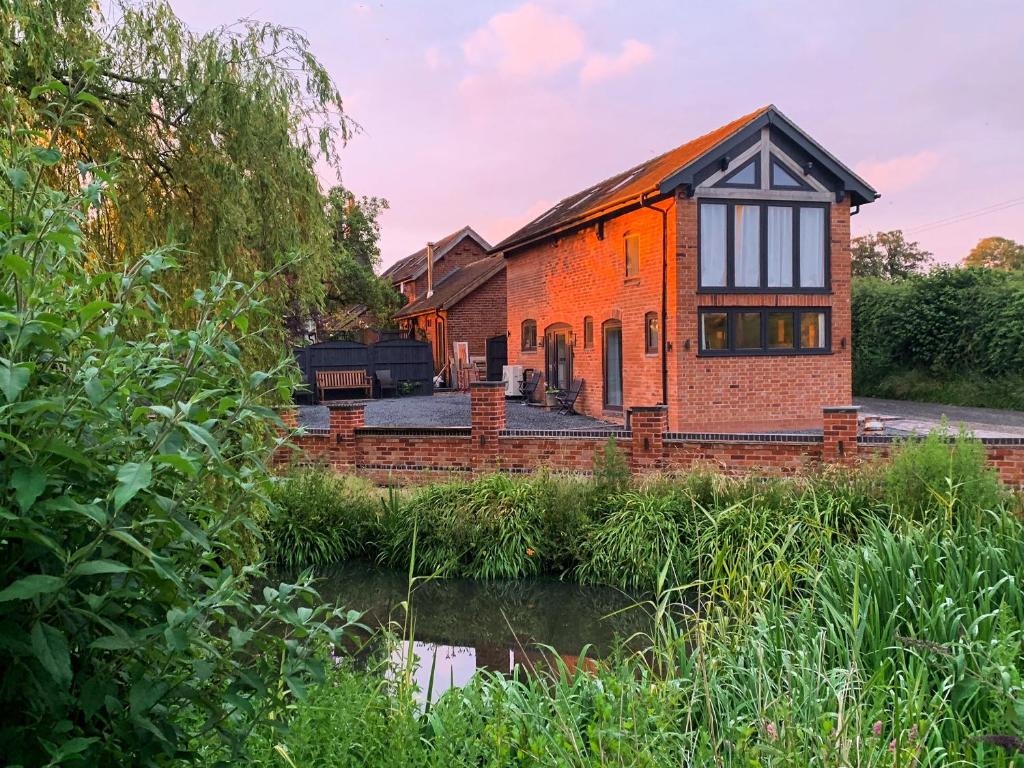 an orange brick house next to a river at The Ash Loft in Audlem