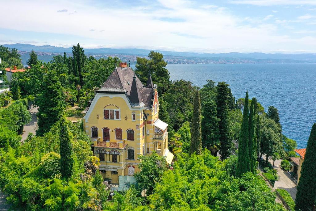 a large yellow house on a hill next to the water at Splendid View apartment Opatija in Opatija