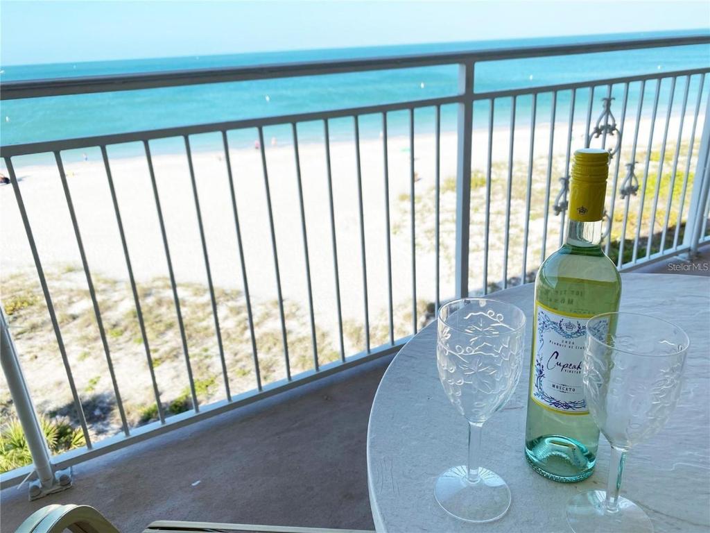 a bottle of wine and two glasses on a table on a balcony at Oceanfront View of Madeira Beach, Steps to the Beach - Madeira Norte Condo in St. Pete Beach