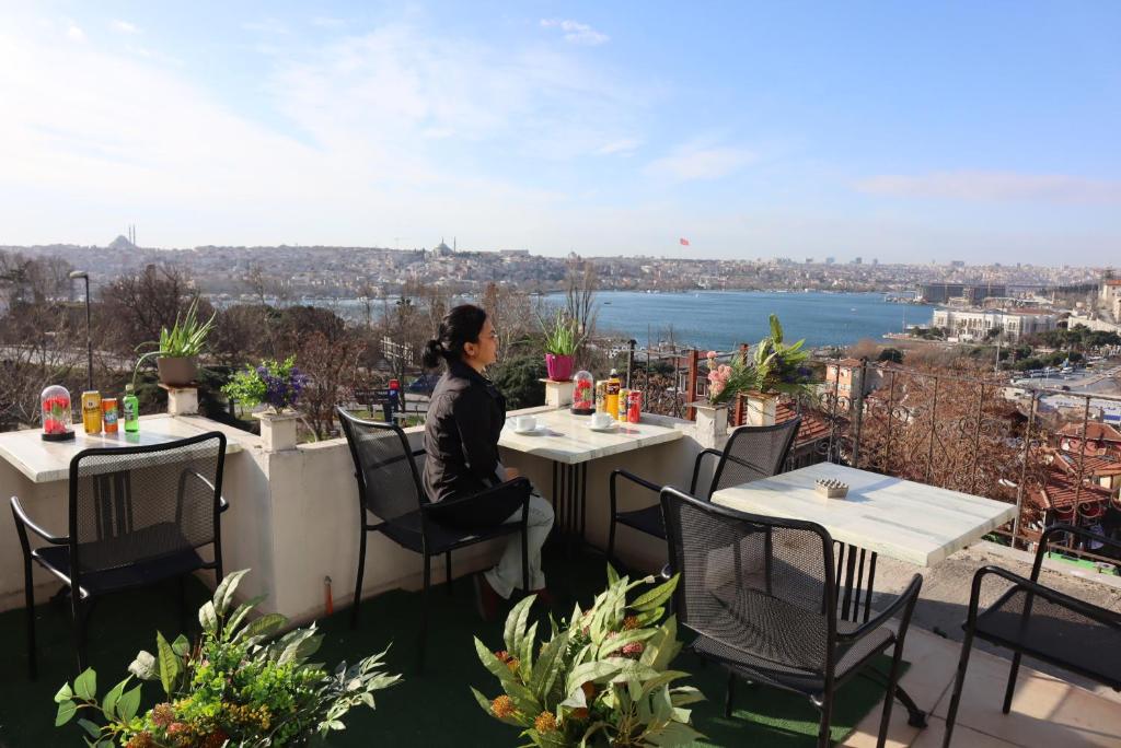 Galata istanbul Hotel في إسطنبول: امرأة تجلس على طاولة على شرفة مطلة على المدينة